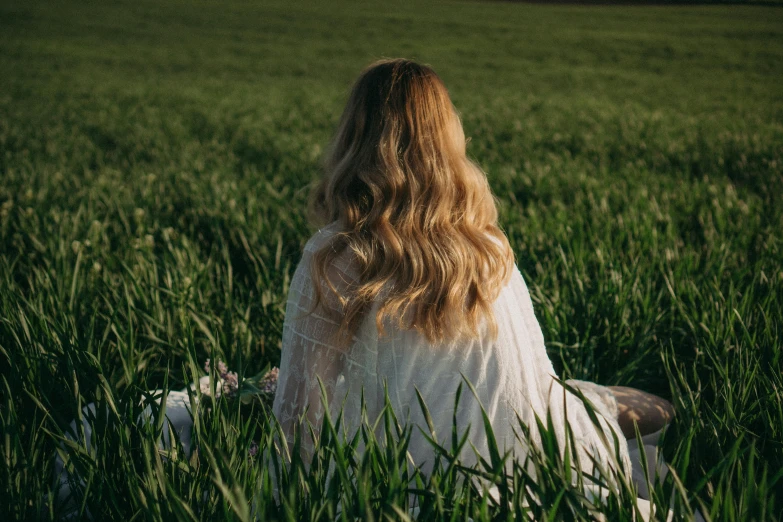 a woman is sitting in tall grass and looking back