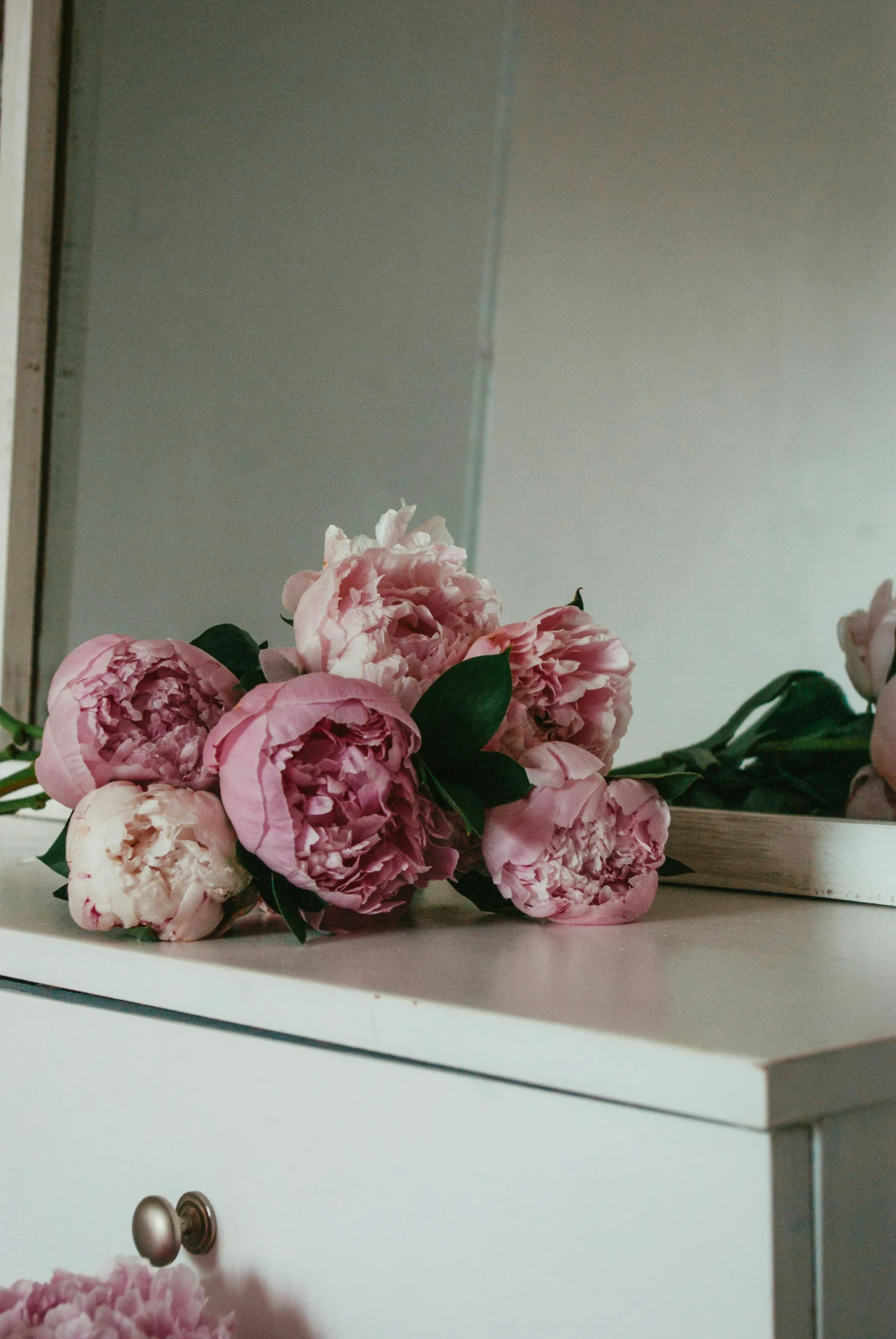 pink peonies are sitting on top of a dresser