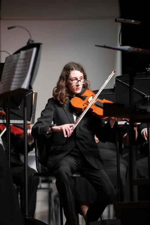 a woman in glasses playing violin while sitting in a chair