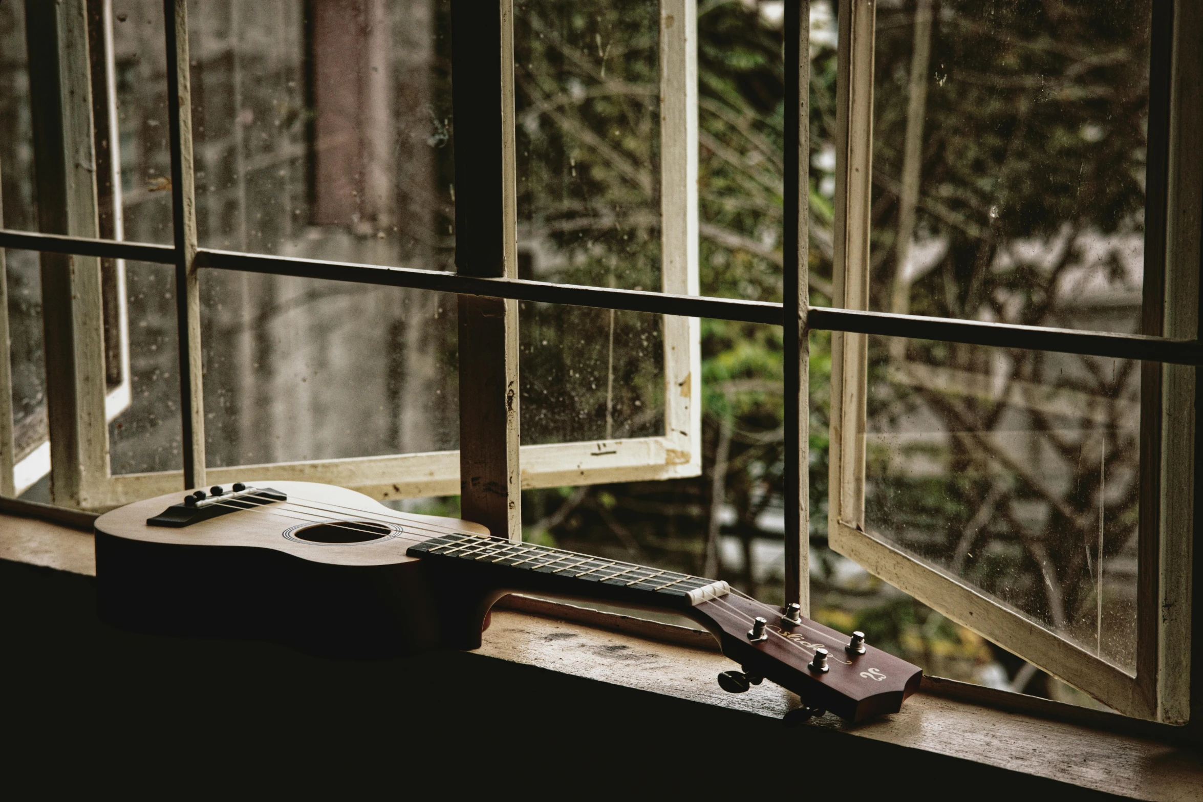 an ukulele resting on the windowsill in front of a window