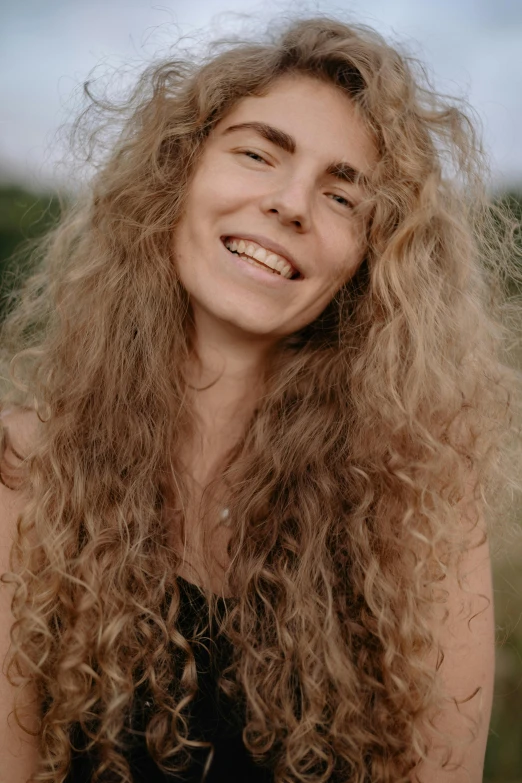 woman with long, curly blonde hair smiles as she stands in a field