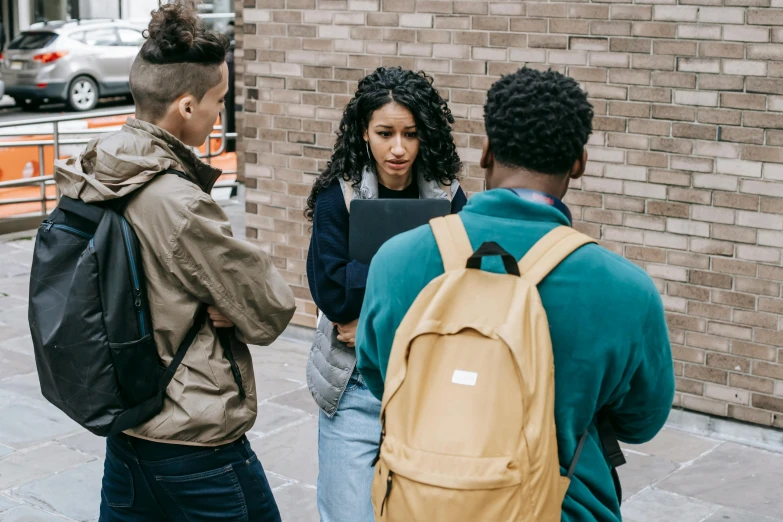 three people stand in front of a brick wall and one looks at his laptop