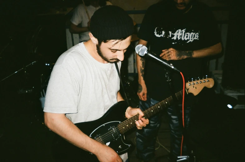 a young man playing the guitar while a young man is singing in the background