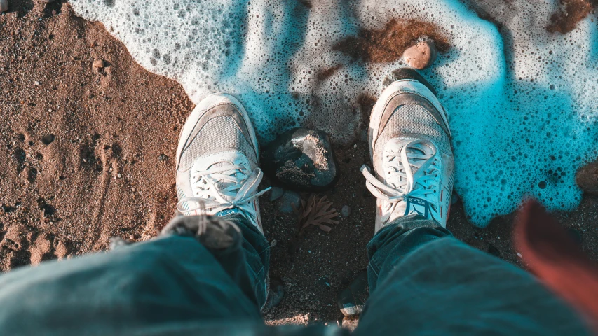 person wearing athletic shoes and pants on top of a sandy area