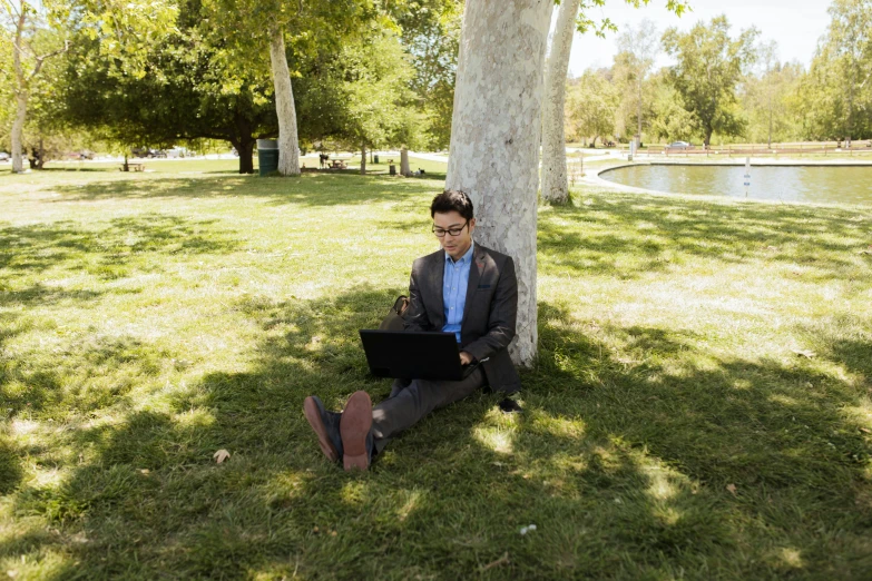 a man sitting in the grass while using his laptop