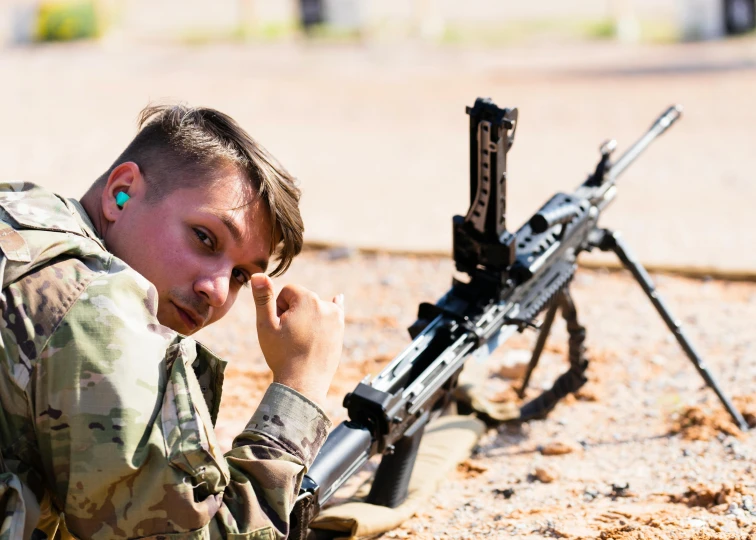 a soldier looking at the camera with a rifle laying beside him