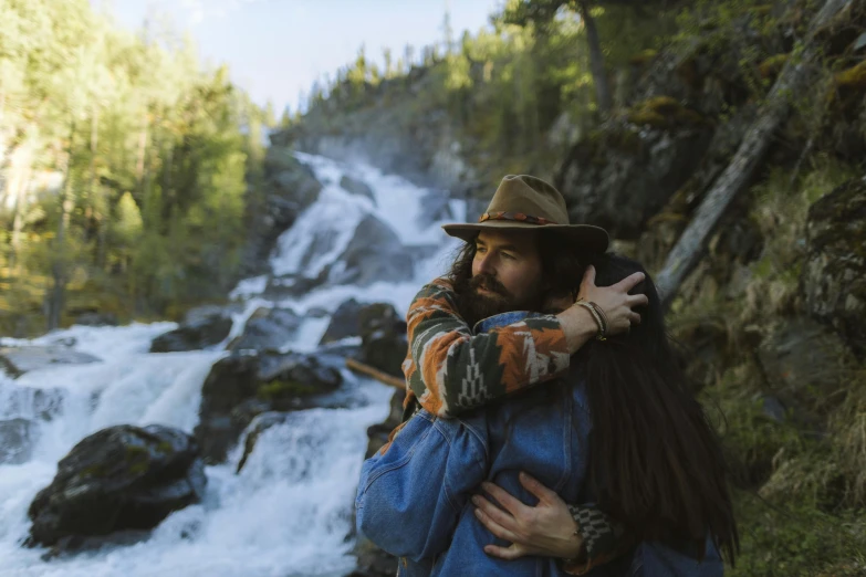 a man is hugging another guy in front of a waterfall