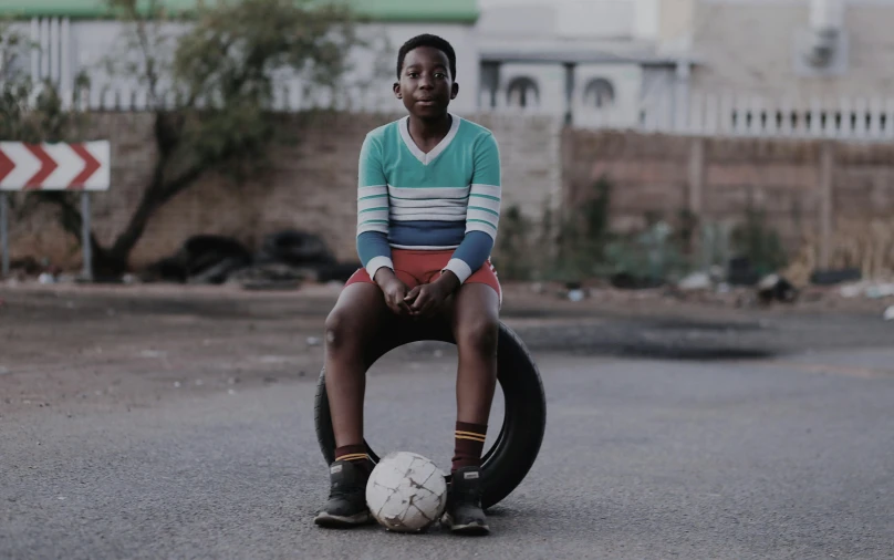 a boy with an ugly soccer ball sitting on a tire