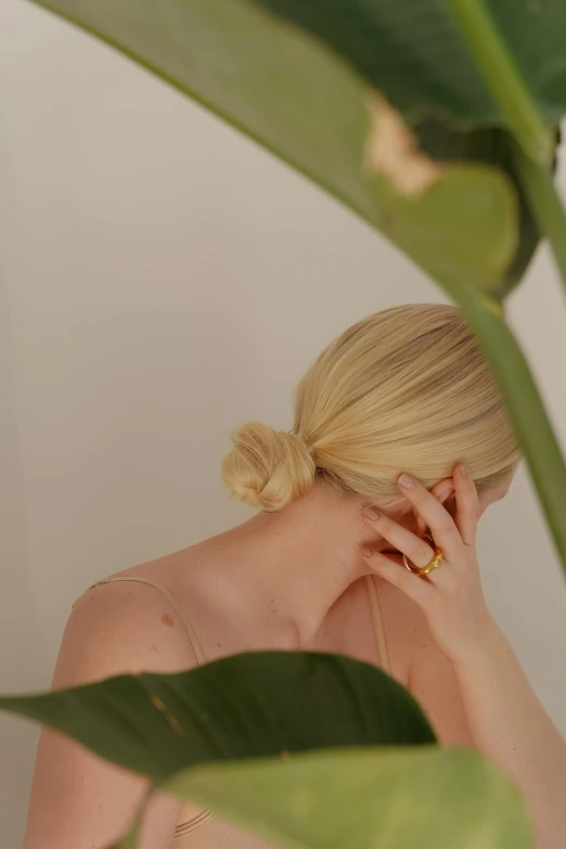 a person wearing a ponytail standing in front of leaves