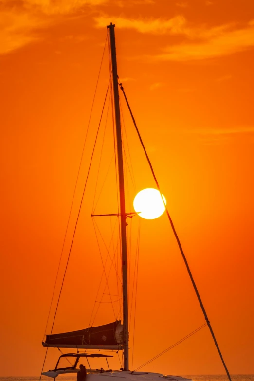 the sun sets on a sailboat in the ocean