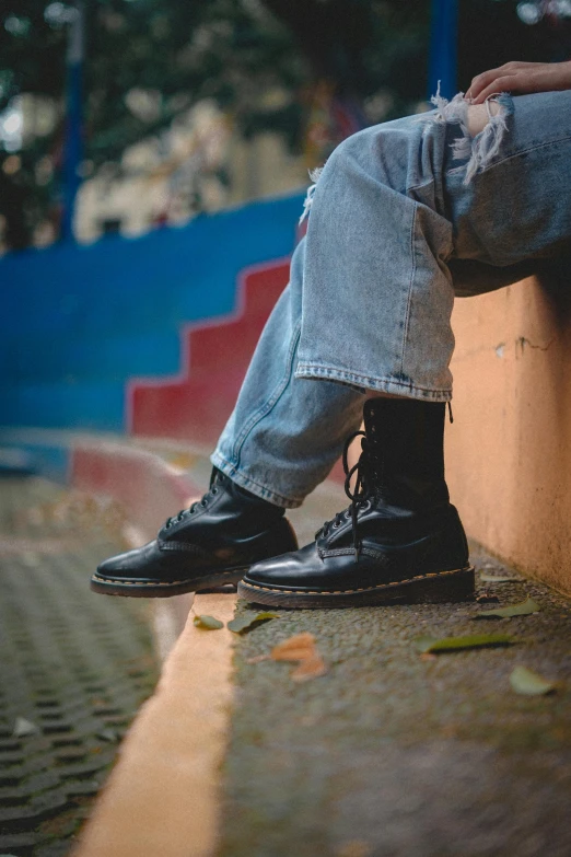 the legs and black shoes of a person leaning against a wall