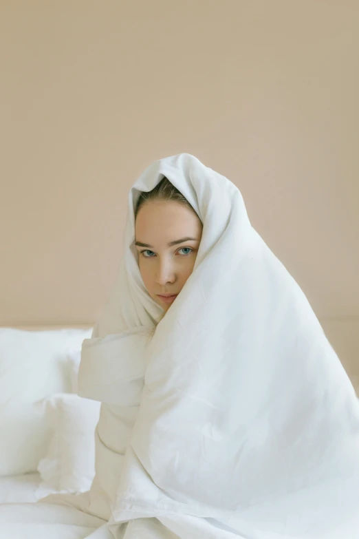 a woman hiding behind white sheets with her head under the blanket