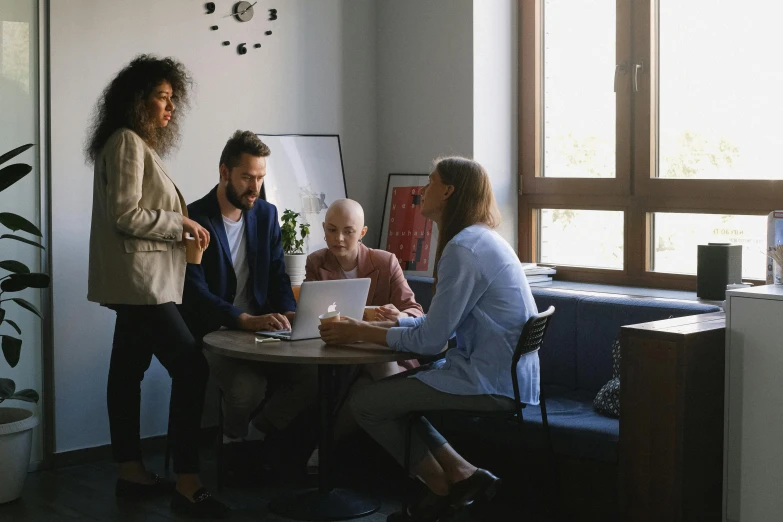 four people sitting around a table with an open laptop