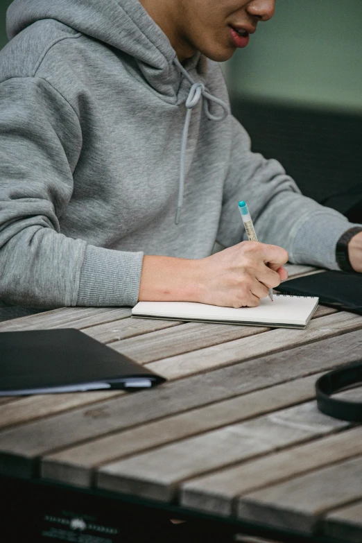 a young asian man is writing on a notebook