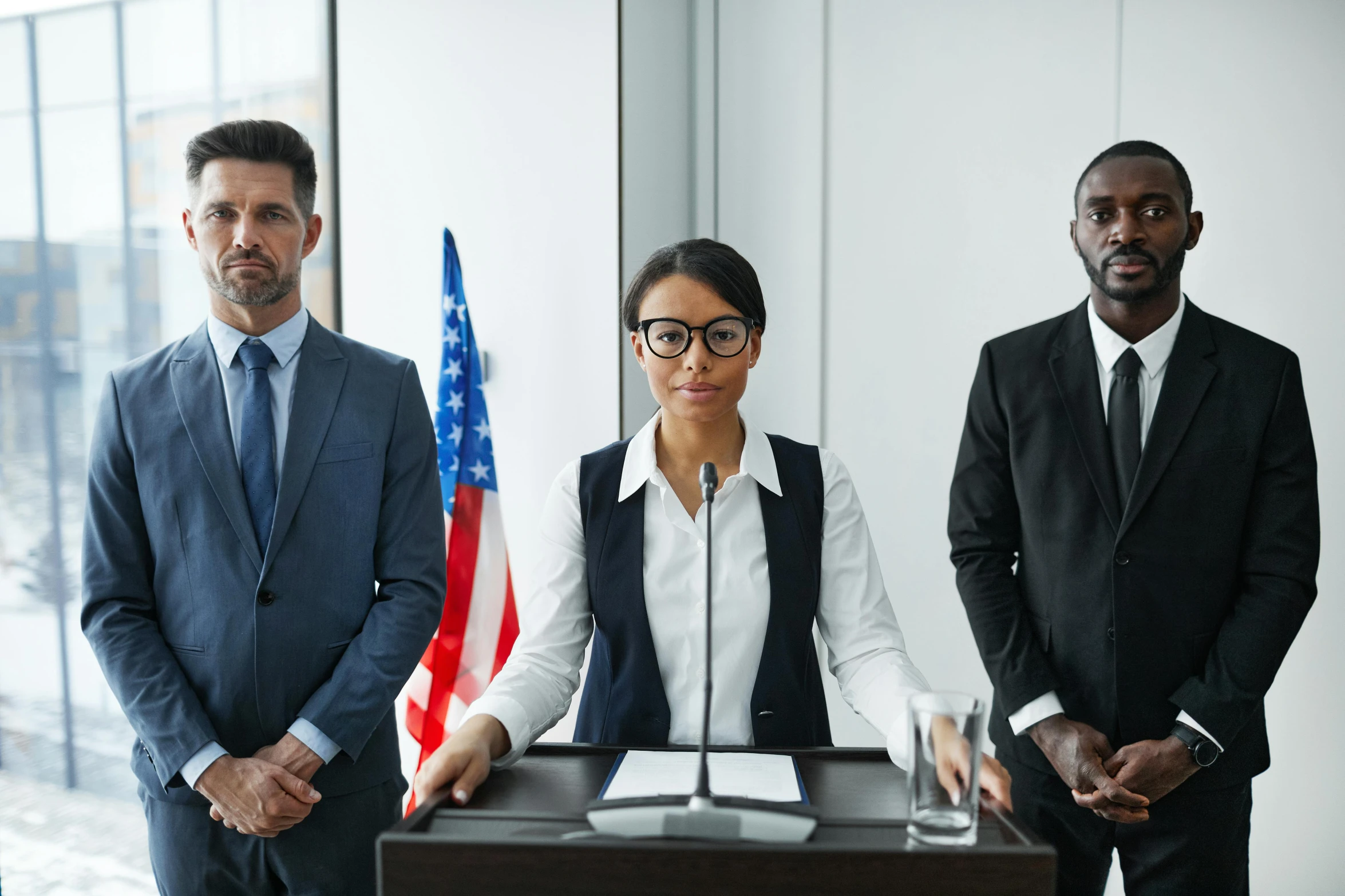 three business people standing in front of a microphone and two flags