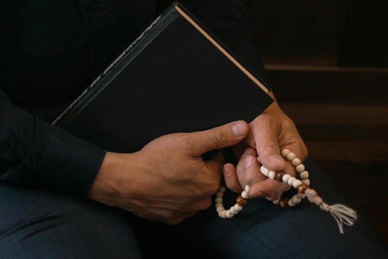 an person is sitting holding a book and rosary