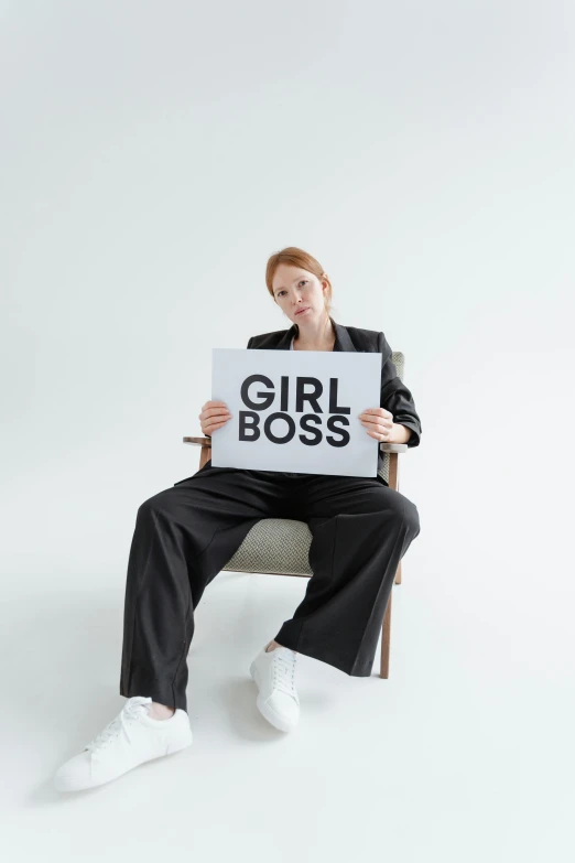 the woman sitting in a chair is holding a sign that says girl boss