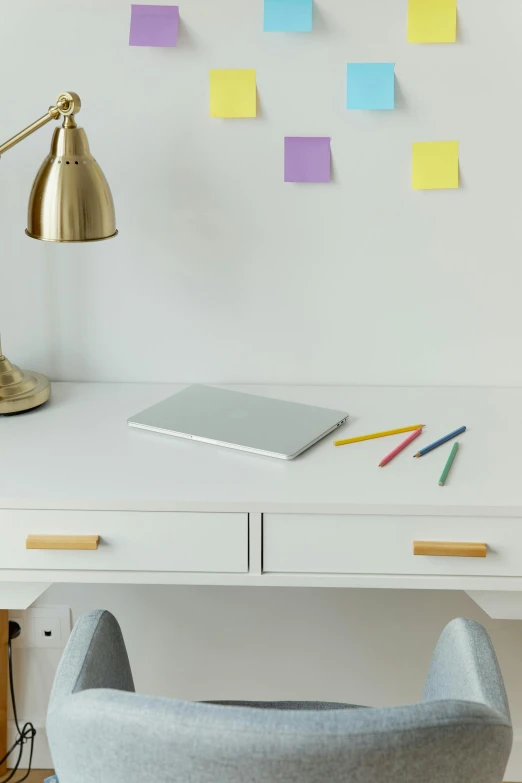 white desk with gold lamp, notepad, and pencils on it