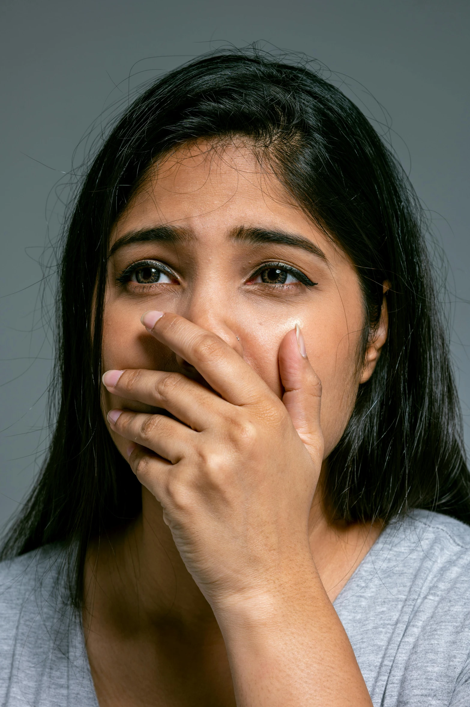 a woman covering her face in front of a gray background