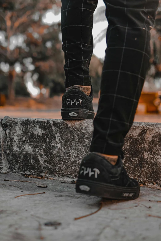 the feet of a person wearing black tennis shoes on a wall