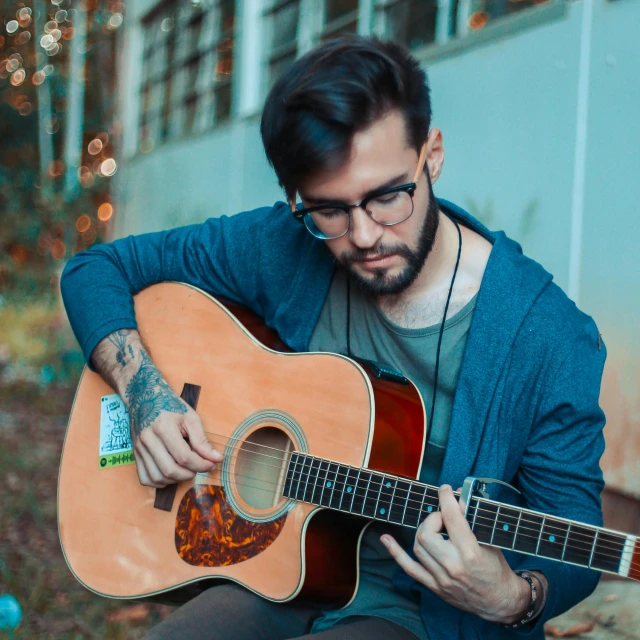 a man playing a guitar in a blue sweater