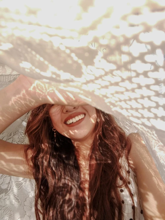 woman with curly hair smiling and holding her head under an umbrella