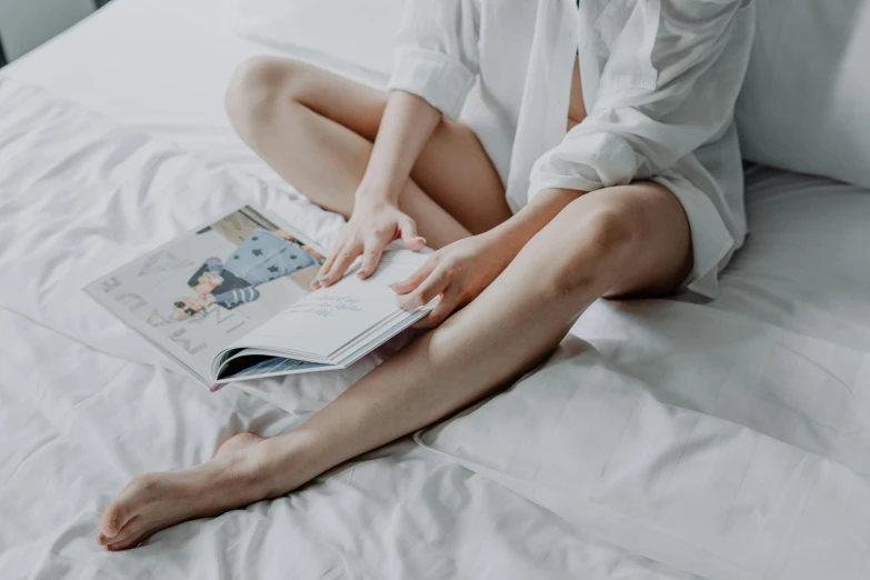 a woman in white shirt sitting on bed reading book