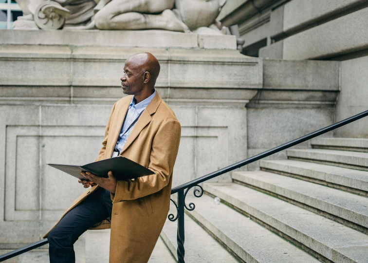 man standing on the steps wearing a coat, reading a book