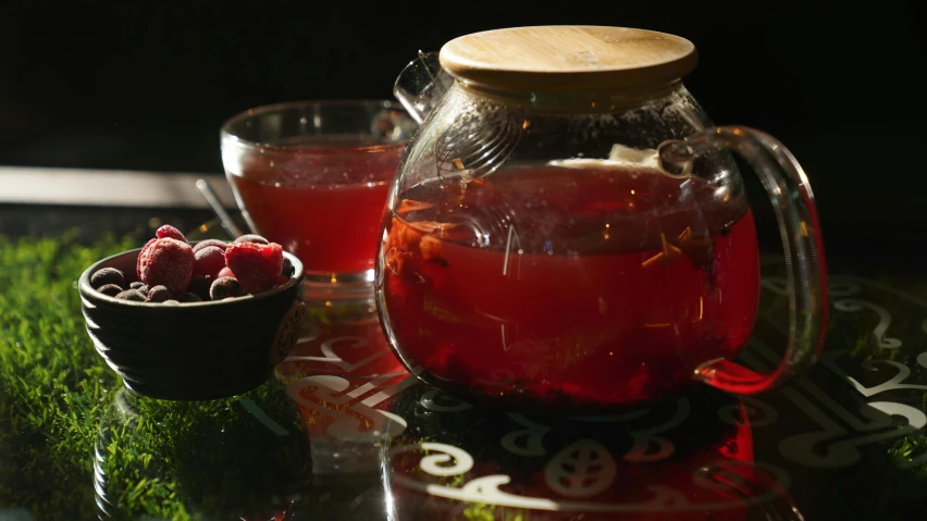 a pitcher of tea sitting next to two cups of berries