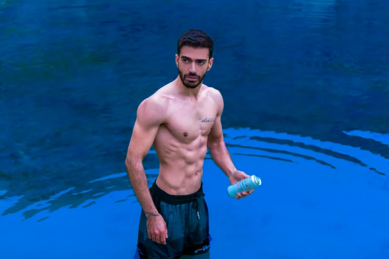 man holding a water bottle in his hand standing in the blue pool