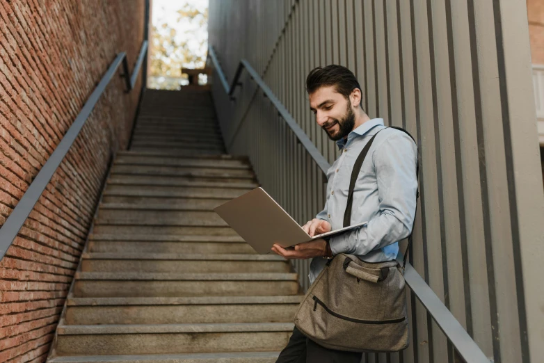 man using laptop outside on stairs smiling