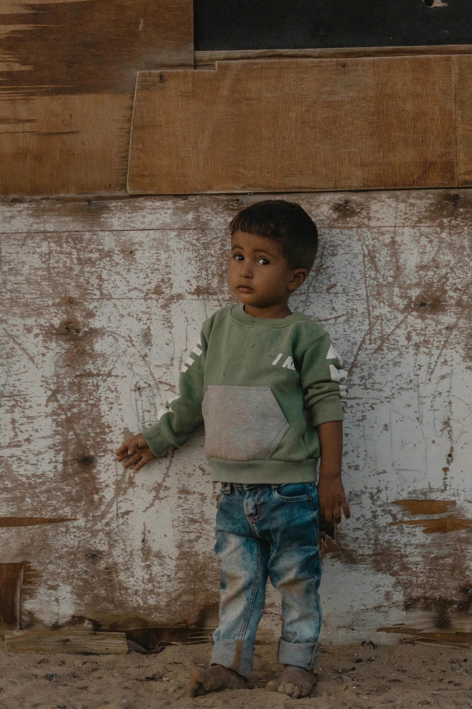 a boy standing against a cement wall with his arms out and looking at the camera