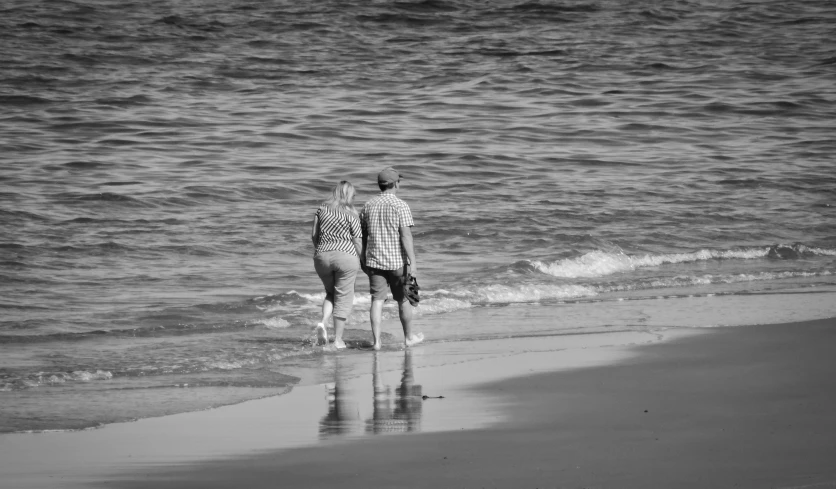 two people are standing on a beach looking at the waves