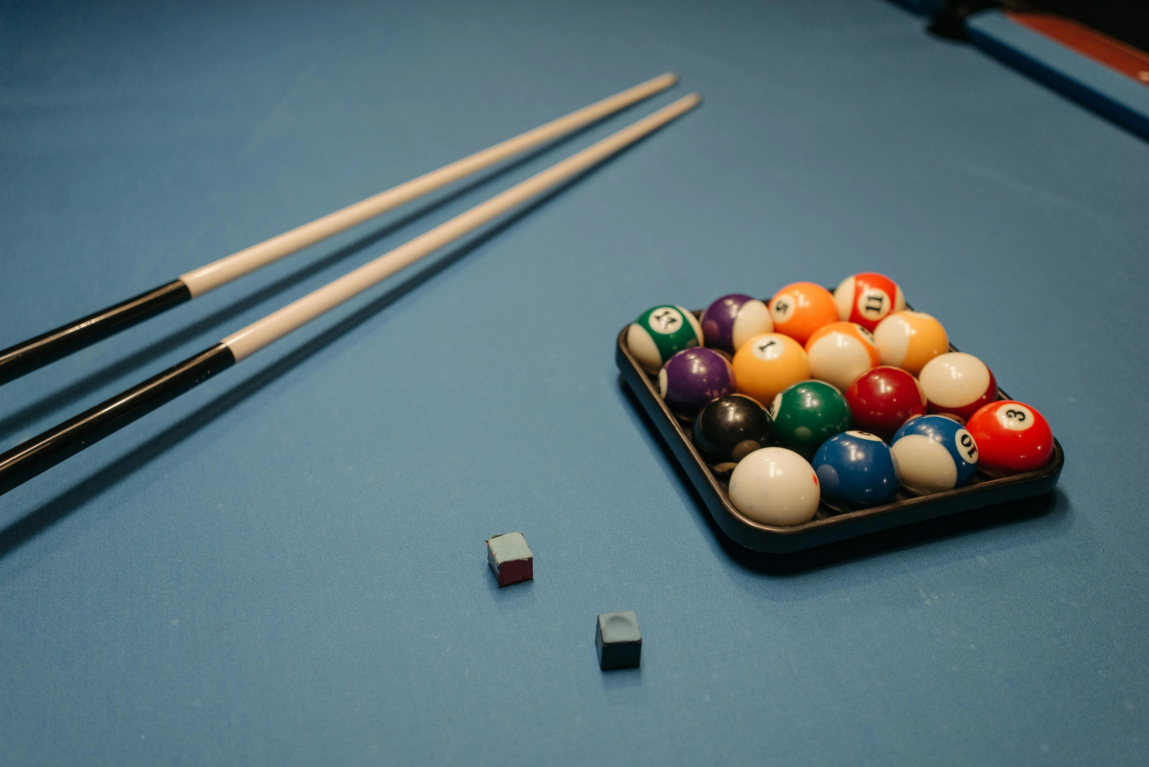 pool balls in a bowl next to two cues