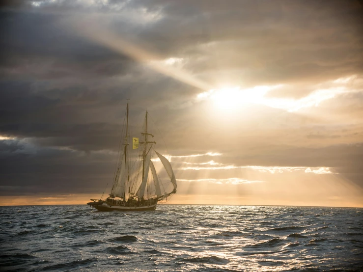 a sail boat sails through the water with sunbeams behind it