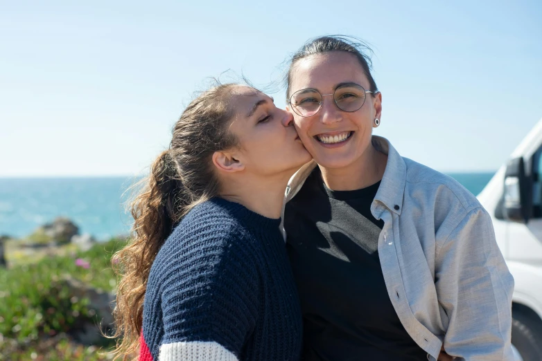 two girls are hugging each other as they stand near the ocean