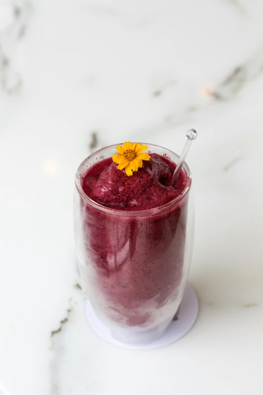 a glass with juice and flowers in it on a white table