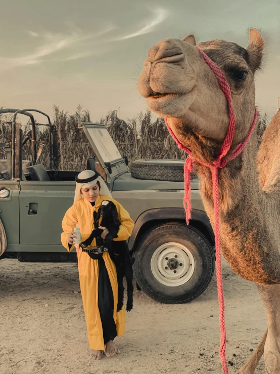a woman standing next to a camel while another girl with a yellow jacket stands beside it