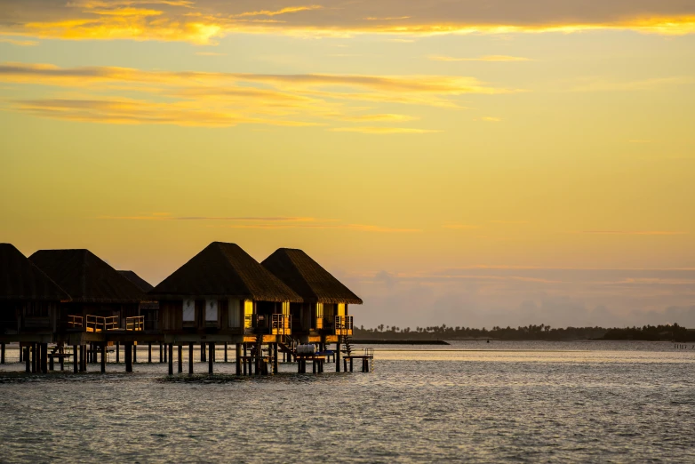 thatched houses in the ocean, during a sunset