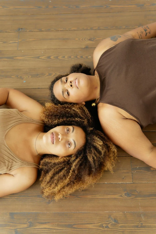 two women lying on wooden floor with their heads together