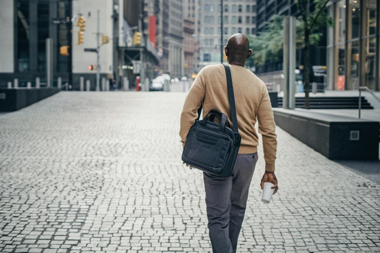 a man in tan shirt carrying bag walking on sidewalk