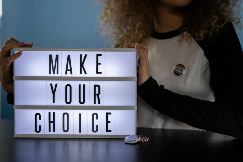 a woman is holding a lighted light box that reads make your choice
