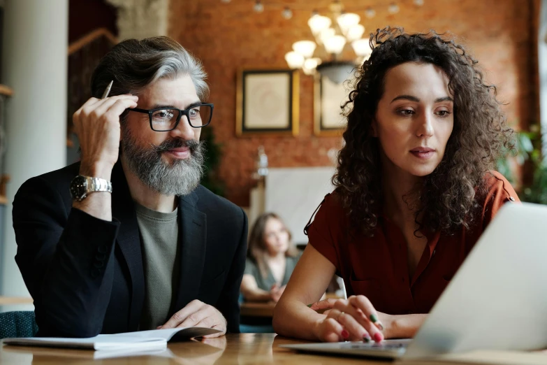 a woman is sitting next to a man at a laptop