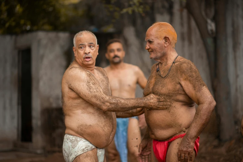 two bald men stand next to each other with mud on their body