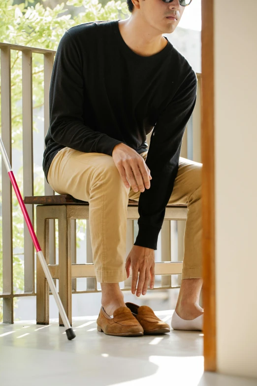 a man with dark glasses sits on a bench wearing slippers