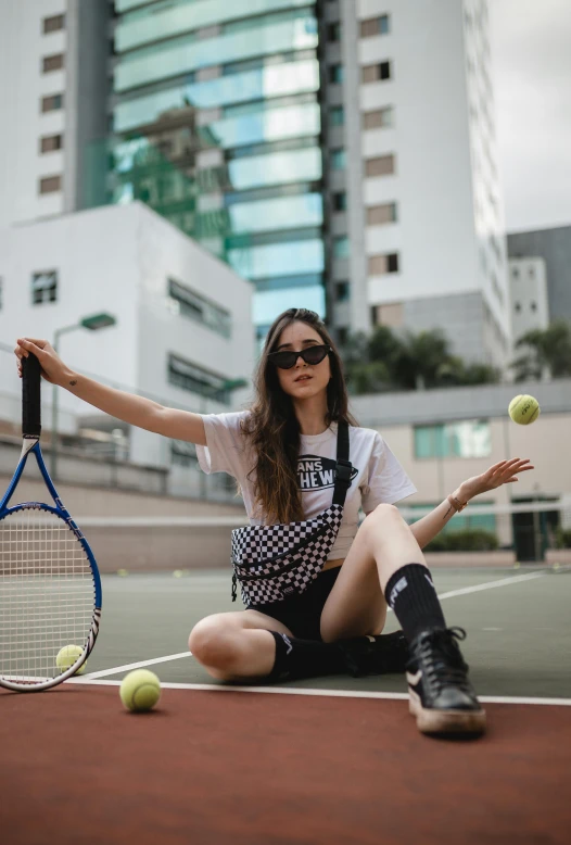 woman with sunglasses sitting on tennis court with tennis racket and balls in air