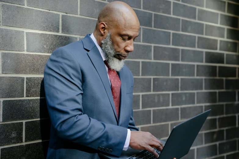 a man is looking at his laptop in front of a brick wall