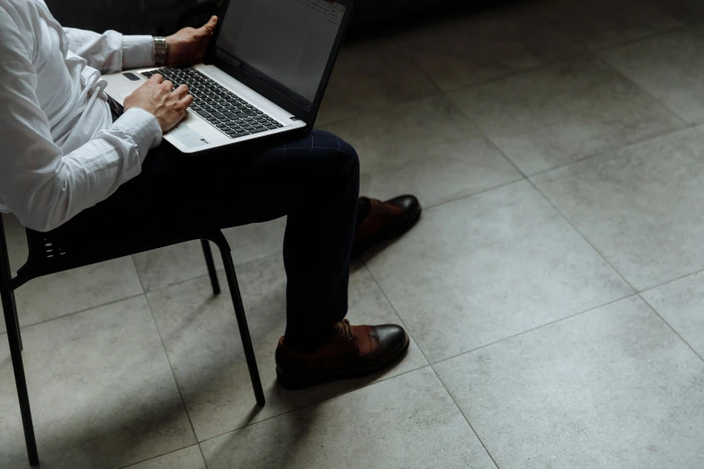 the man is sitting down typing on his laptop