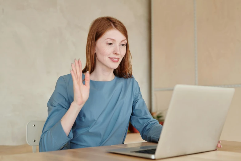 a red haired woman waving in front of her laptop