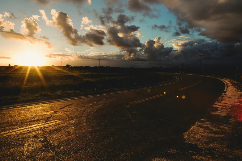 a view of the sun rising over the horizon from the side of a highway